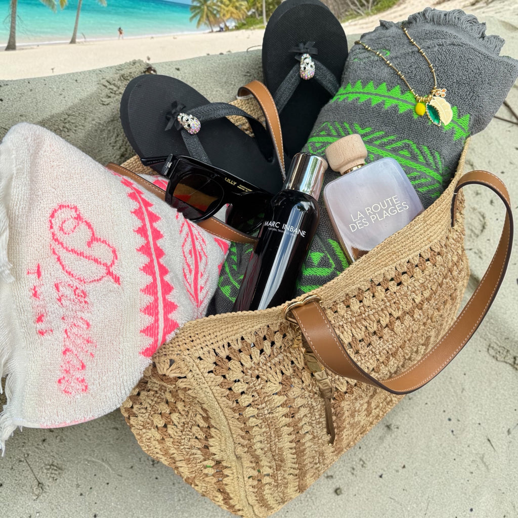 She Stories Devotion handdoek met borduursel in een strandtas met slippers en accessoires op het zand